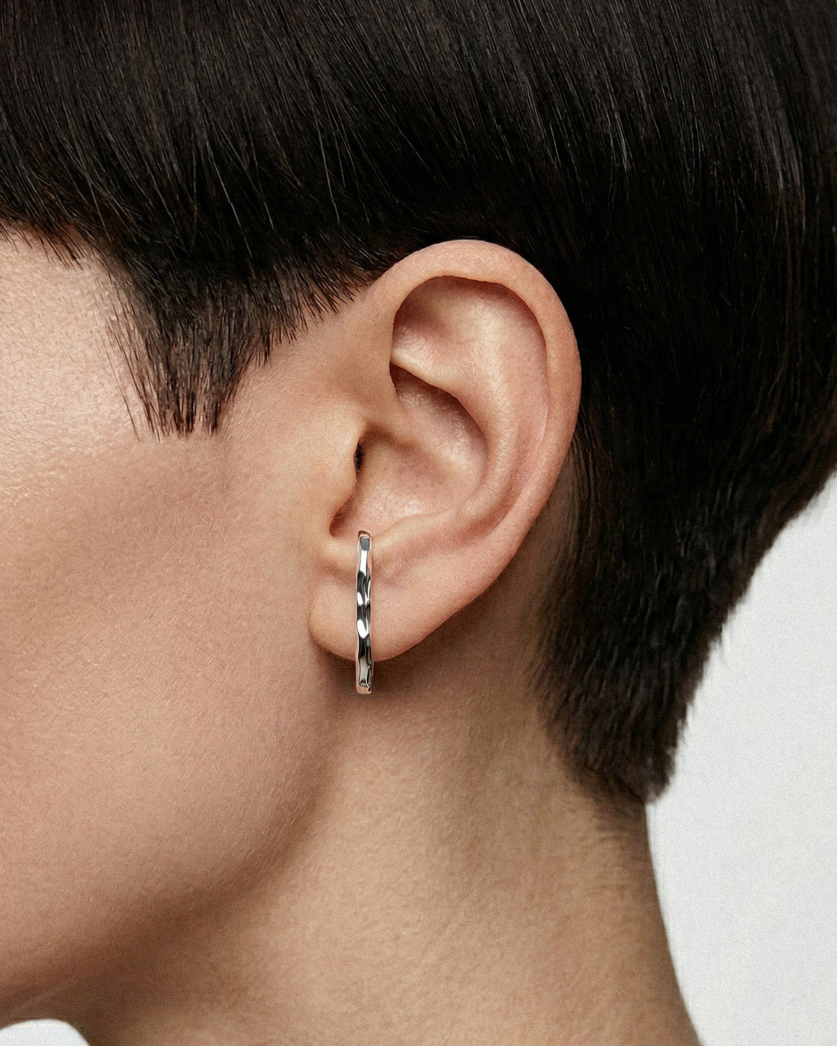 Close-up of an ear wearing a silver slim earring curving up and inside the ear