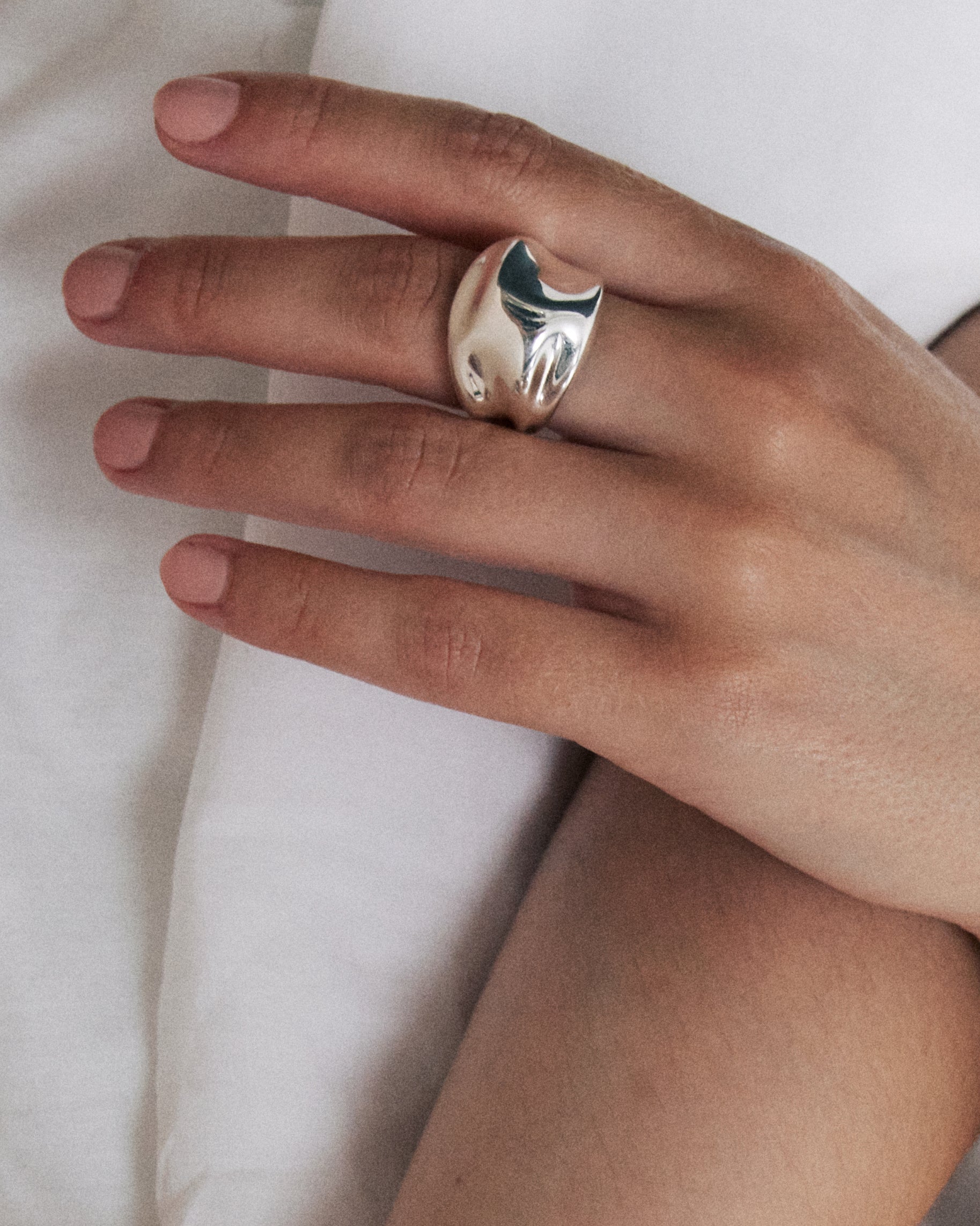 Hand wearing a uniquely designed silver ring, resting on a white shirt