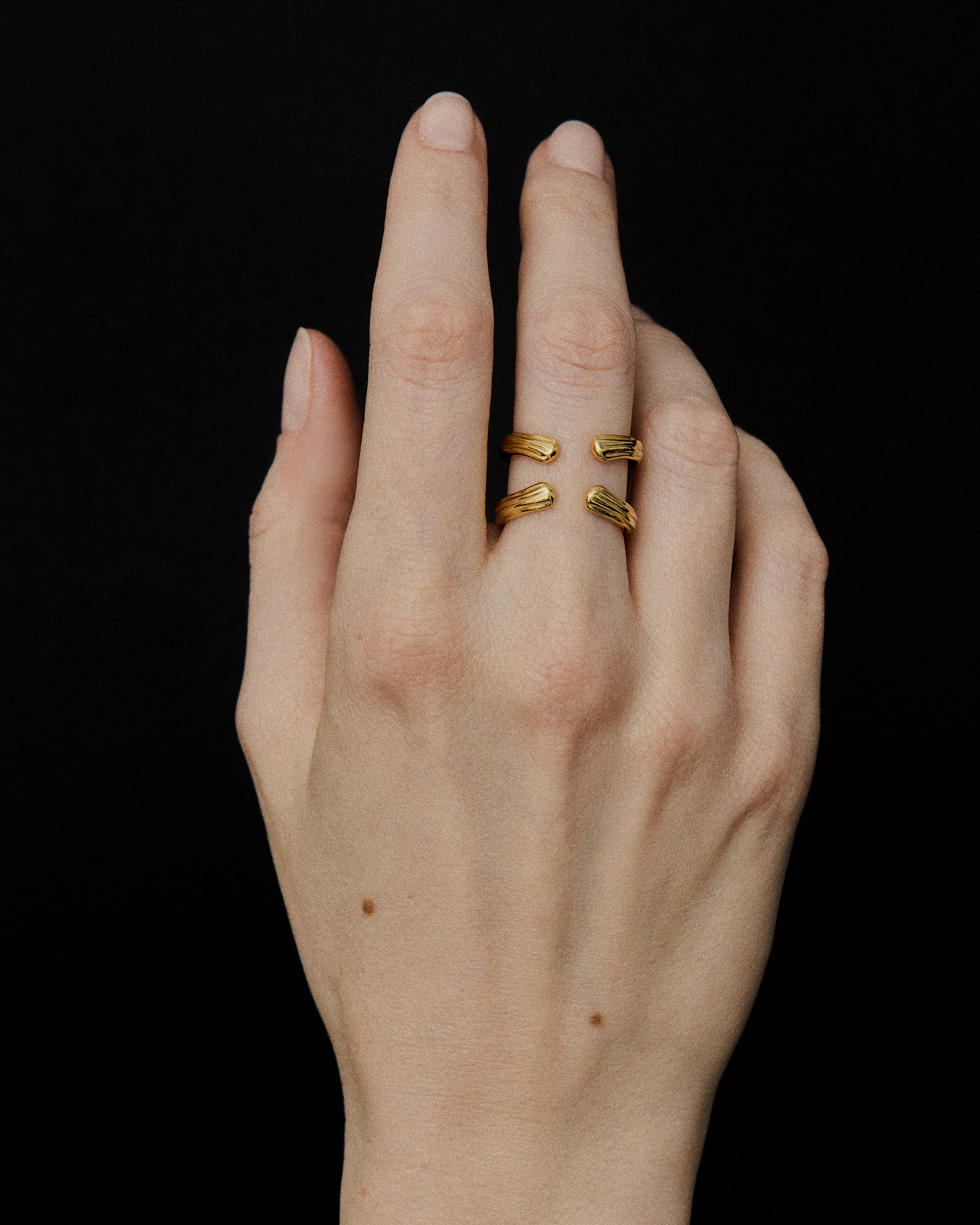Close-up of a hand wearing Double Flow 18k solid Gold Ring with four sculptural open arms and curved flowing surfaces