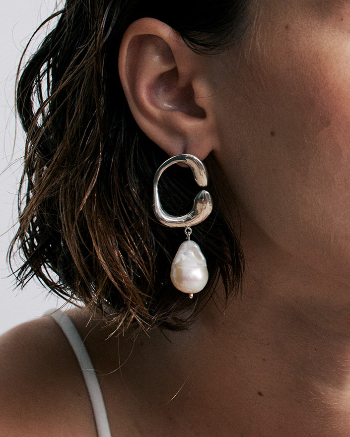 Close-up of an ear wearing a silver hoop earring with a white freshwater pearl drop