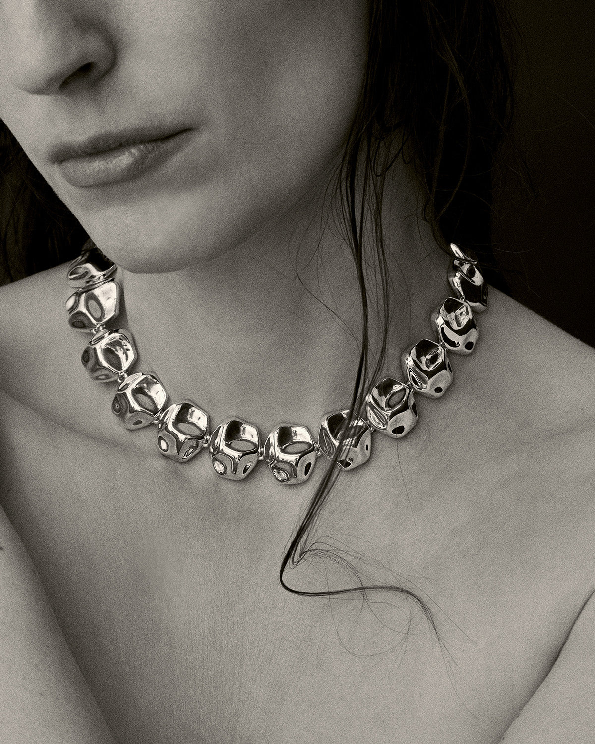 Black and white close-up of a model wearing a silver cosmic necklace with chunky reflective beads, styled as a bold statement necklace