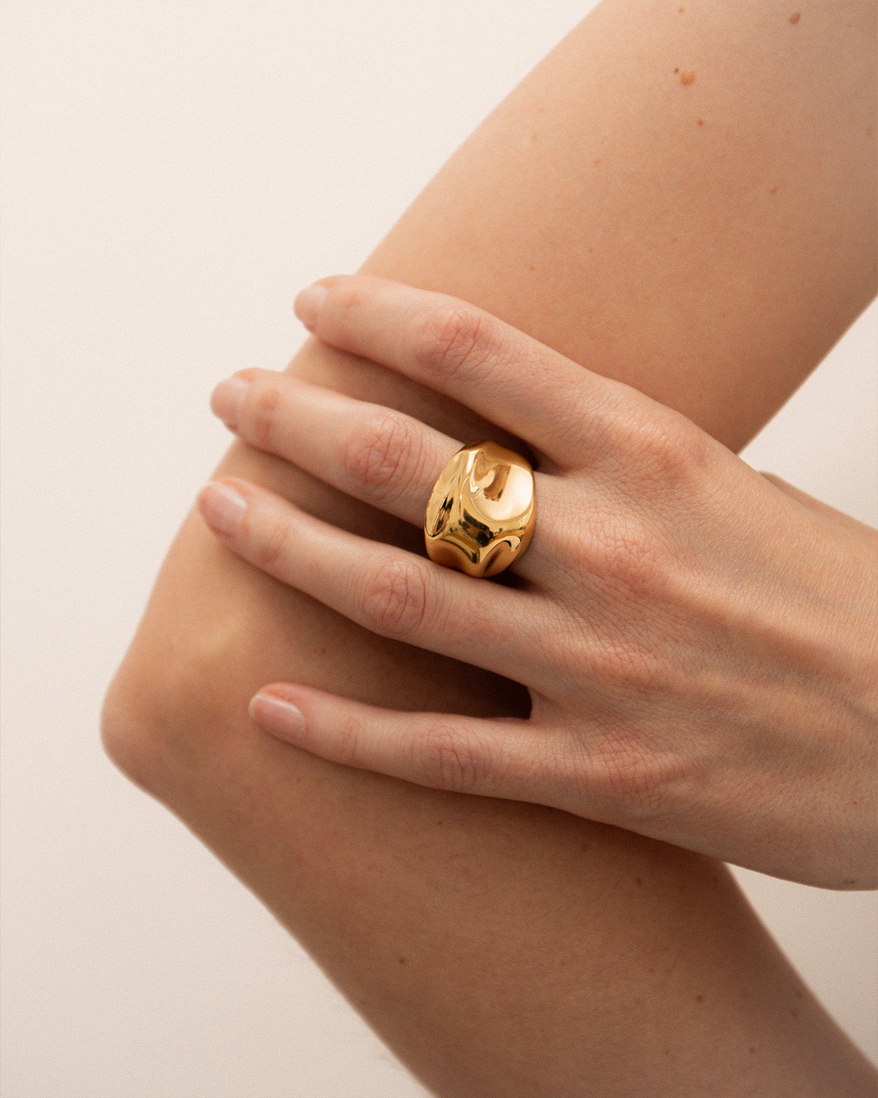 Gold vermeil organic ring on a hand against a beige background