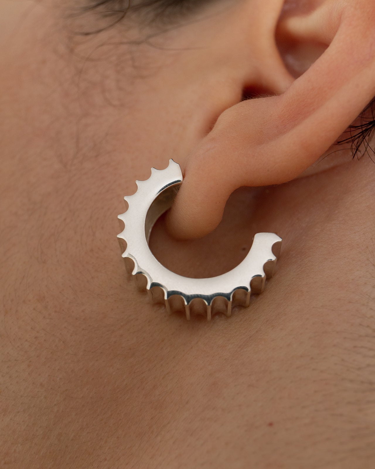 A close-up image of a person wearing a large silver hoop earring with etched grooves like an ancient roman column.