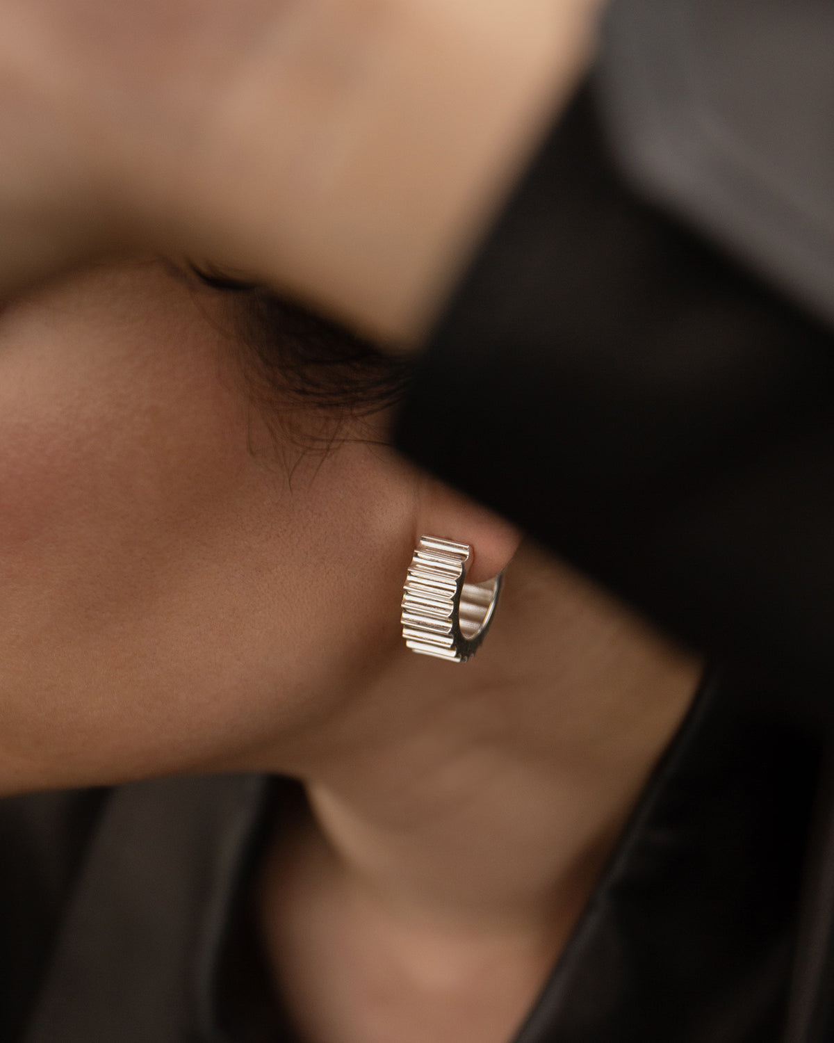 An image of a person wearing a large silver hoop earring with etched grooves like an ancient roman column.