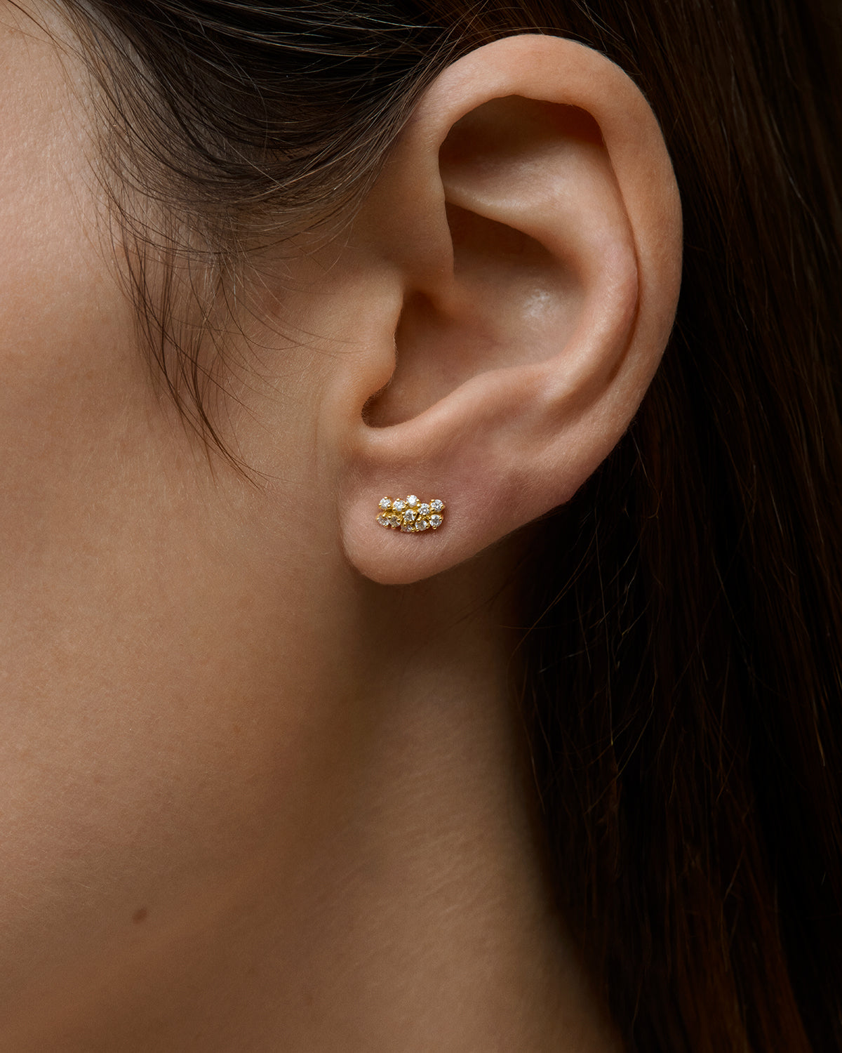 Close-up of an ear wearing 18k gold diamond stud earrings