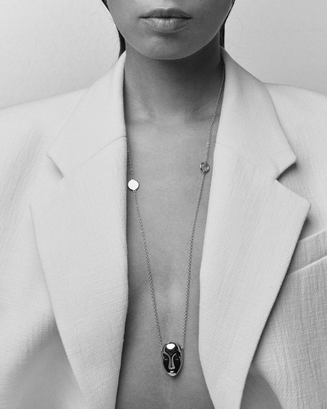 Una persona con un collar con colgante escultórico con forma de rostro en plata, con una chaqueta blanca