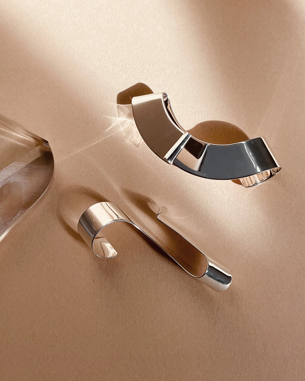 Minimal ring still life featuring a bold sculptural silver ring with a high-shine reflective surface, styled on a warm neutral background in soft light